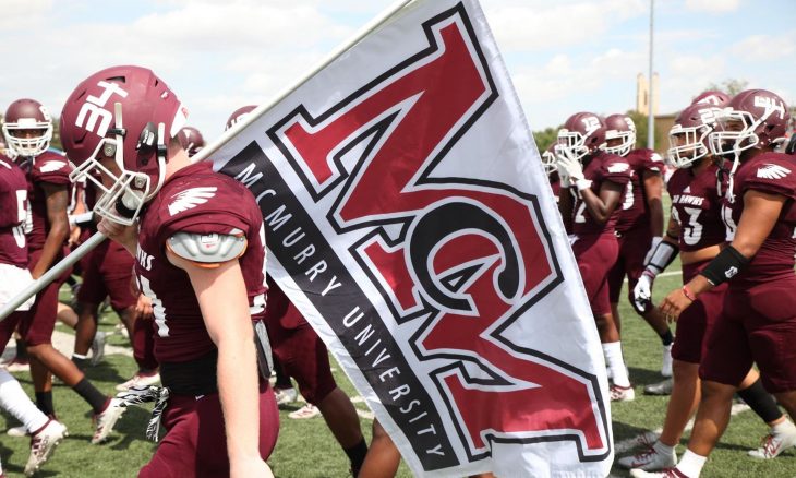 football players carrying the McMurry Flag