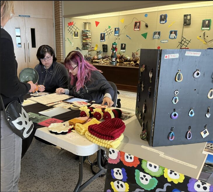 student purchases art at table with two student workers